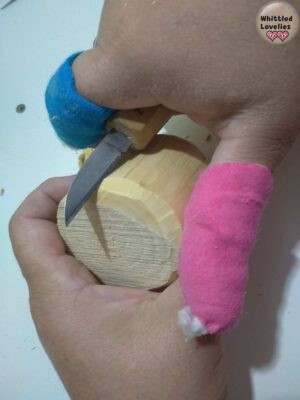Two hands holding a piece of wood from a branch. A knife is used to start rounding off the sides.