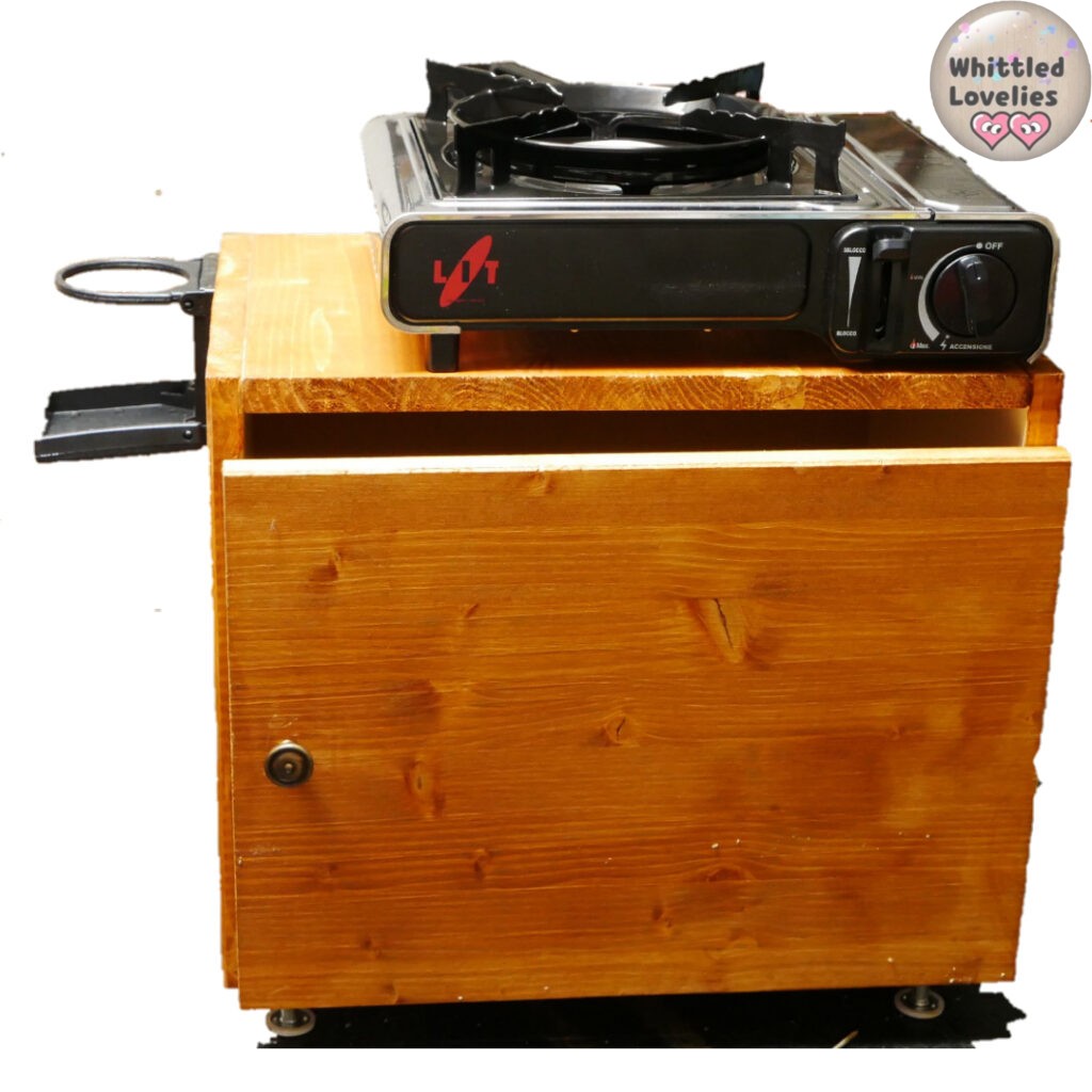 DIY Camping Box tutorial: how to make it, the featured image shows a wooden cabinet, with a knob curtain and a glass holder on the side. It can be used as a base for a camping stove or as a table.